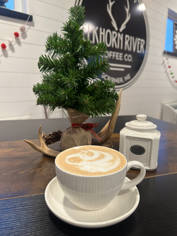 Coffee cup sitting on top of a table with holiday decorations behind it inside of the Elkhorn River Coffee Company.