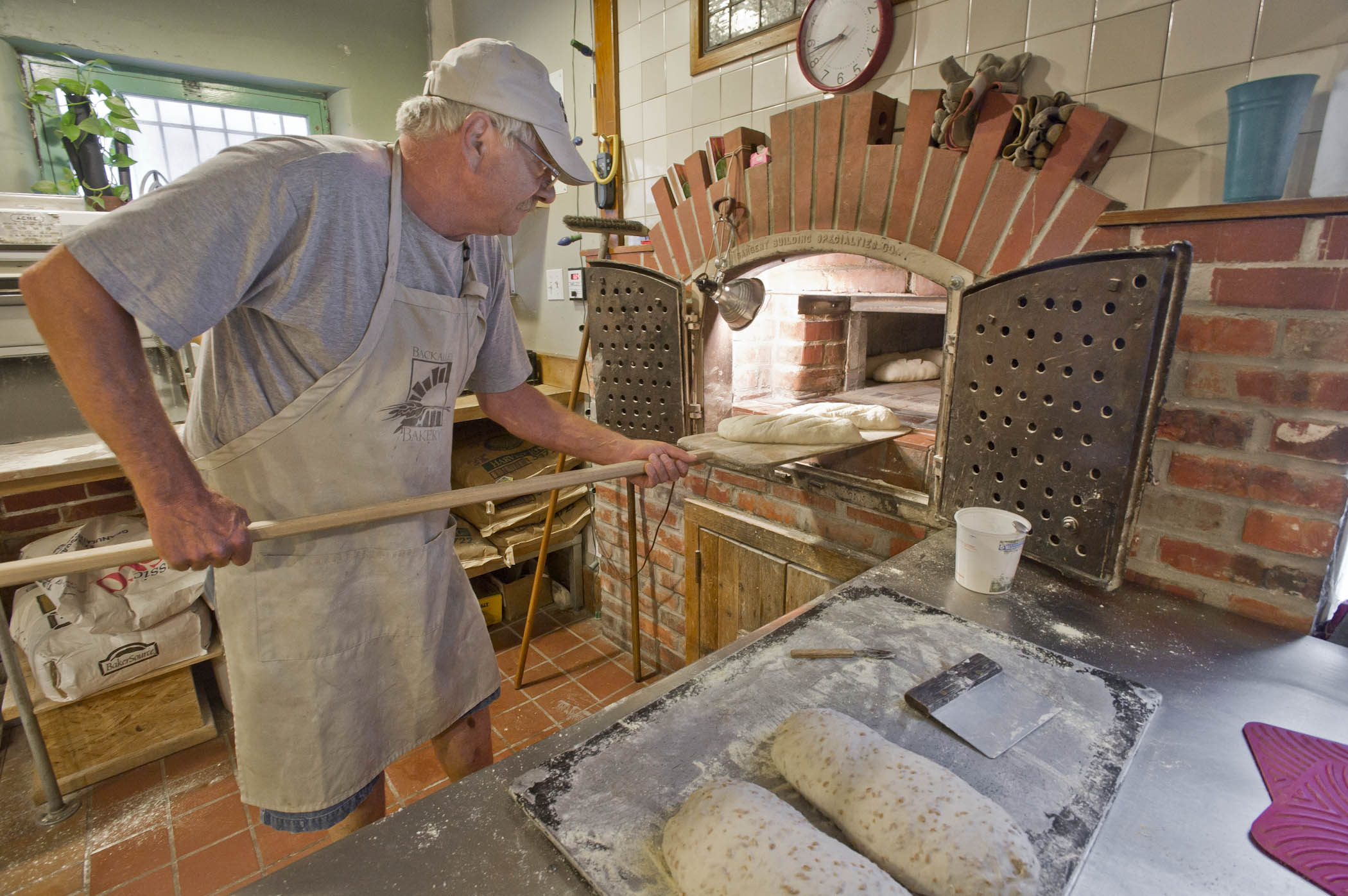 A baker placing dough in the brick oven at Back Alley Bakery.