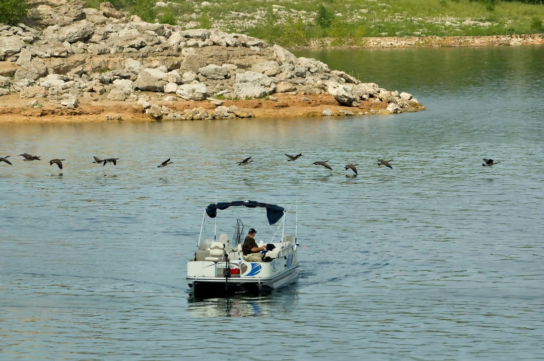 A man fishing from a boat on Lake McConaughy as a flock of birds flies past just above the water.