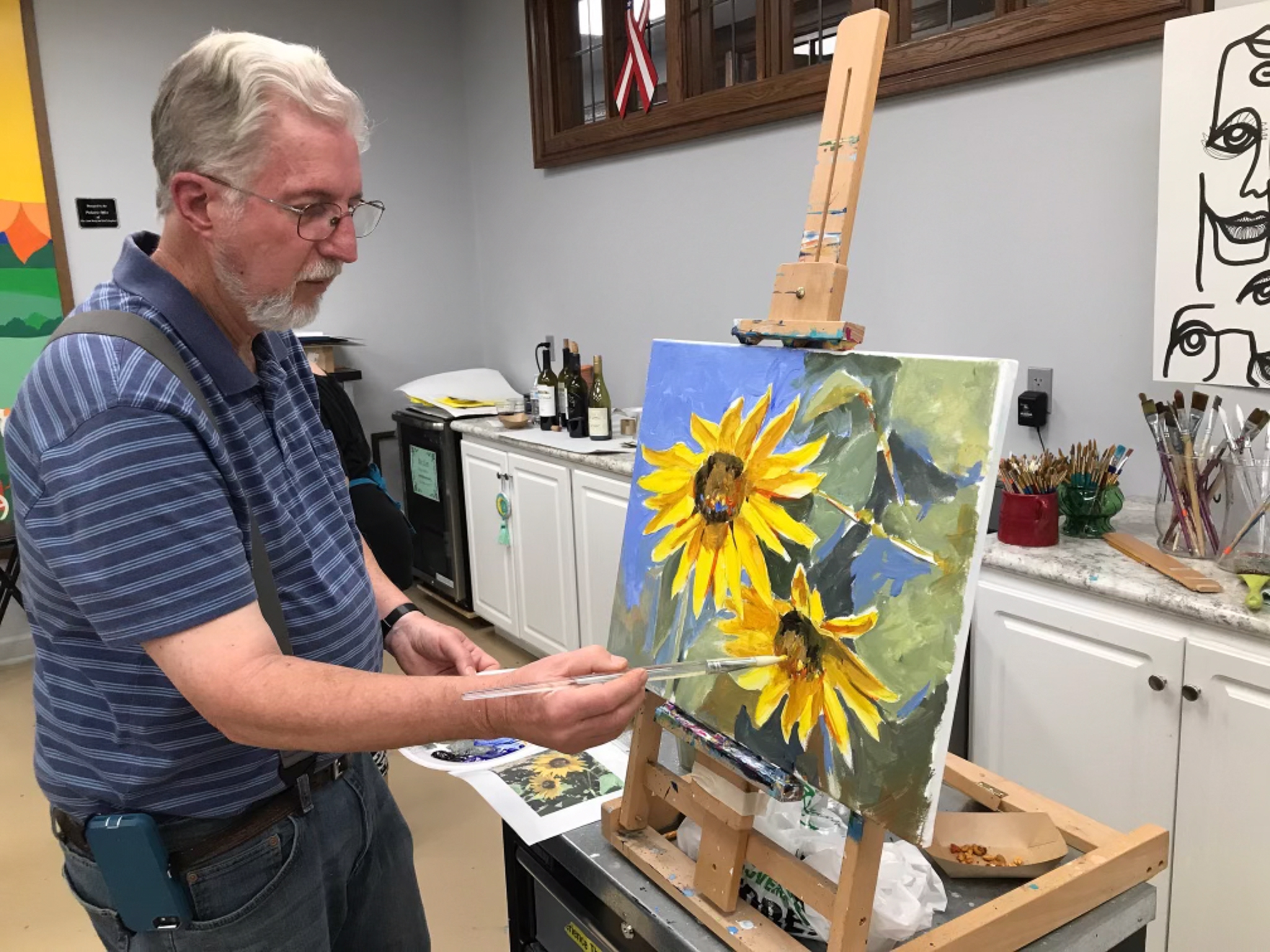 A man painting a picture of flowers at Prairie Arts Center.