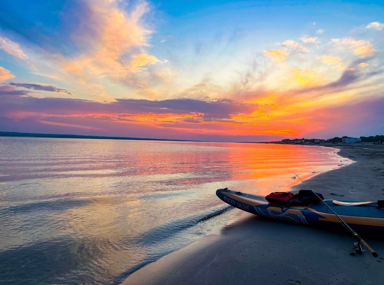 A paddle board and fishing pole on the shores of Lake McConaughy at sunset.