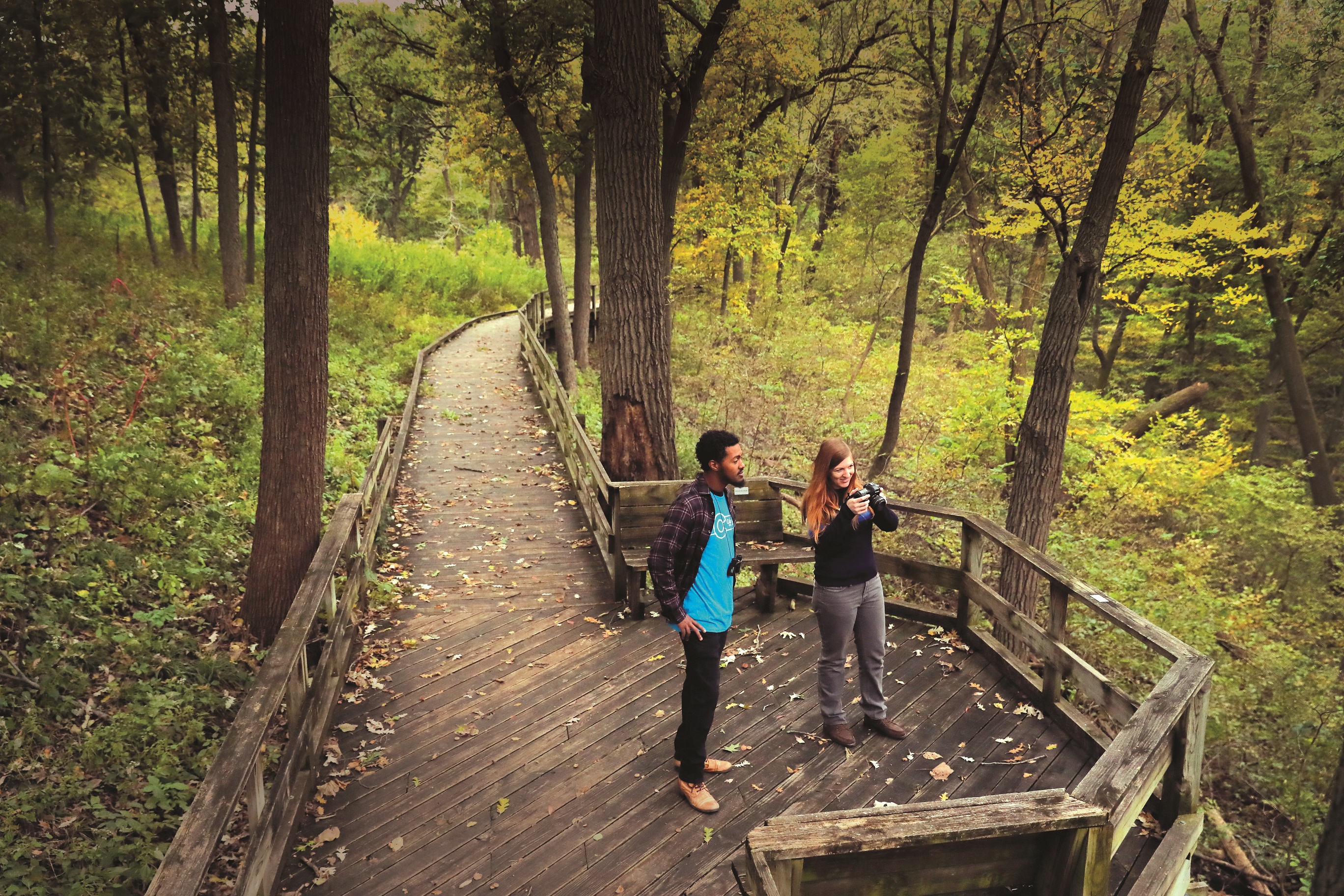 Two people taking nature photos from the boardwalk surrounded by trees at Fontenelle Forest.