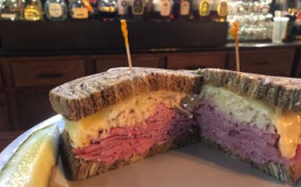 A Reuben sandwich plated with a bar behind it.