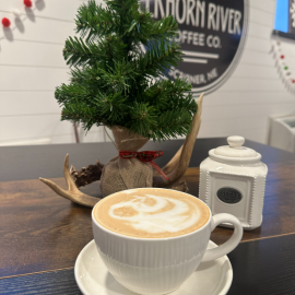 Coffee cup sitting on top of a table with holiday decorations behind it inside of the Elkhorn River Coffee Company.