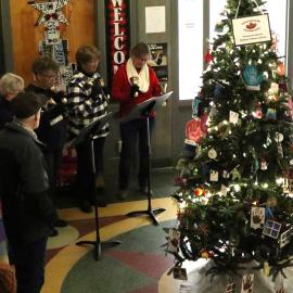 A group of women sing Christmas carols surrounding a Christmas tree.