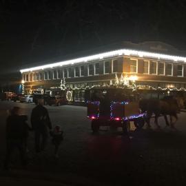 A decorated sleigh with people riding in behind a horse outside of the Shops at the Victor Anderson Building.